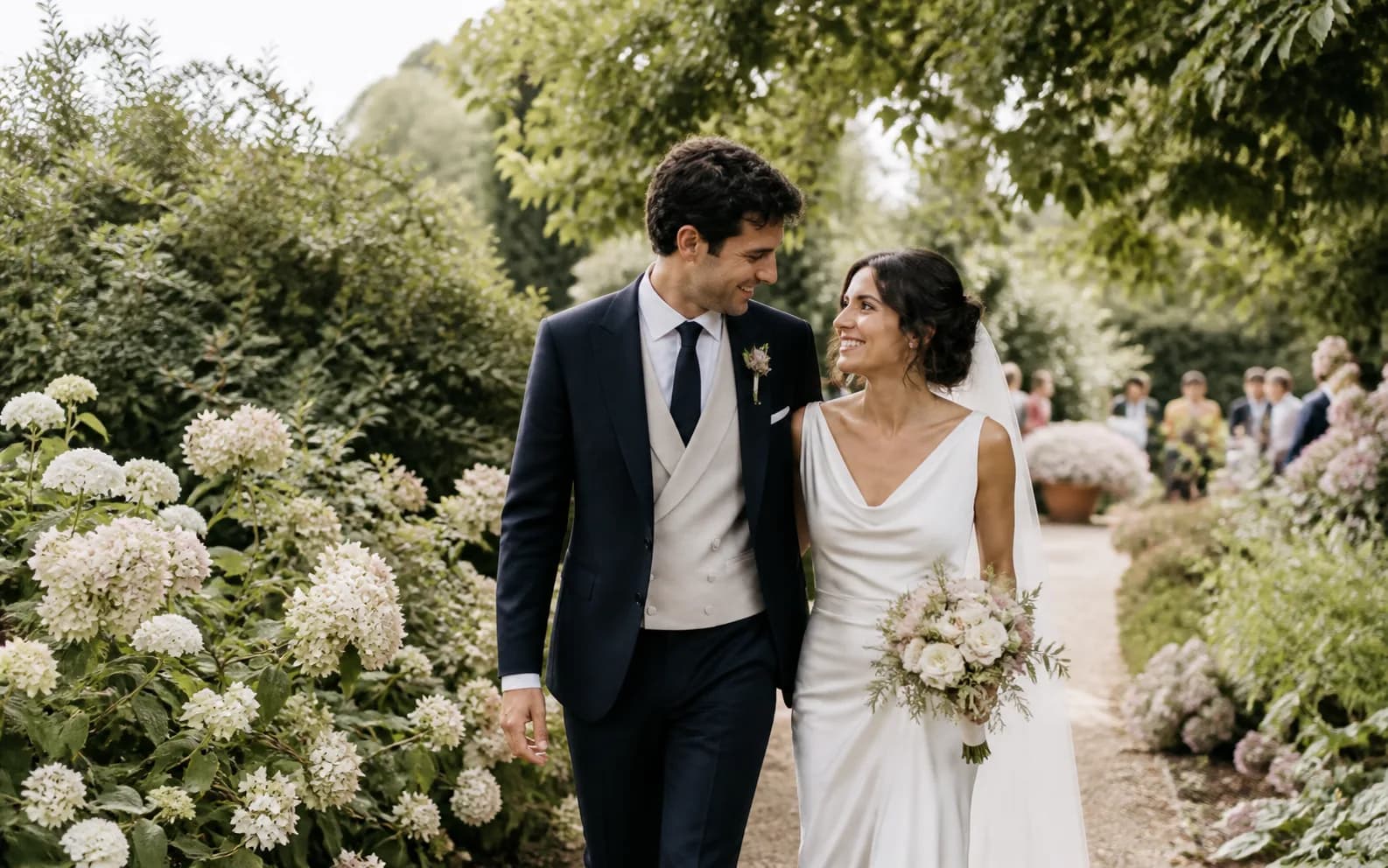 A newly married couple walking together through a garden in warm afternoon light
